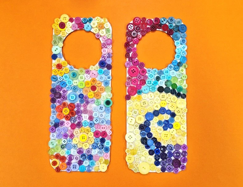 Two crafted button art door hangers lying side by side on an orange background.